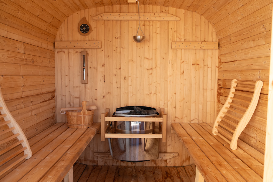 Warm, minimalist timber sauna interior with wooden benches and a stone heater glowing softly, low ambient lighting, steam faintly visible, calm and premium wellness photography, wide shot